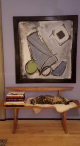 Photo of a cat lounging on a bench under a painting.