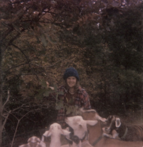 Teenage girl standing next to a tree, surrounded by goats